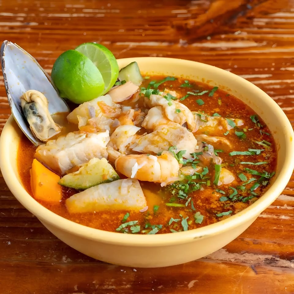 A vibrant Mexican seafood soup with fish, shrimp, mussels, and vegetables, garnished with lime and cilantro.